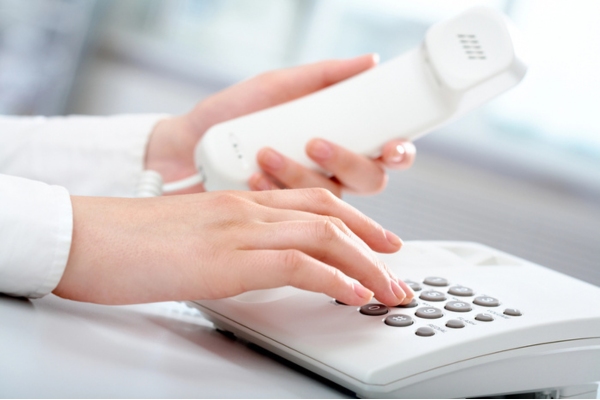 cropped view of a woman's hand dialing on a home phone depicting calling a professional HVAC contractor