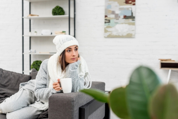 woman keeping warm with coffee and full winter outfit indoors depicting compromised heating system