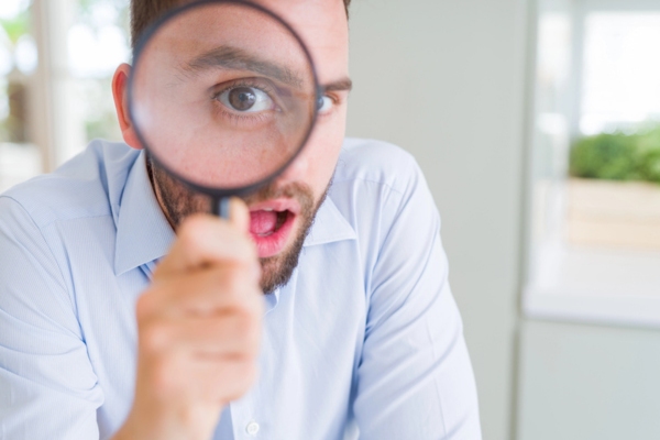 man looking through a magnifying glass depicting inspecting home for drafts & air leaks