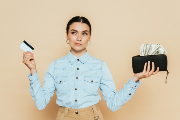 woman thinking while holding card and wallet with cash on separate hands depicting financial considerations for Ducted vs. Ductless Air Conditioners