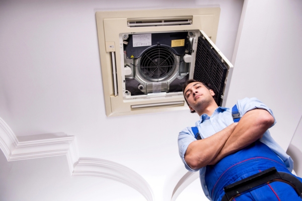 HVAC technician standing below an air conditioner indoor air handler