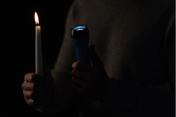 burning candle and flashlight held by a man depicting difficulty starting a standby generator