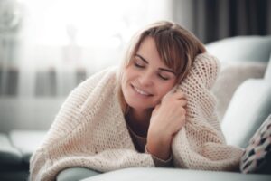woman feeling cozy while hugging knitted blanket during winter