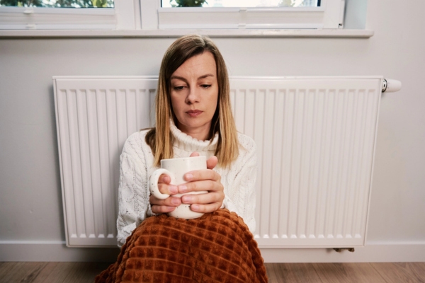 woman feeling worried staying by the heating oil radiator due to low supply during storm