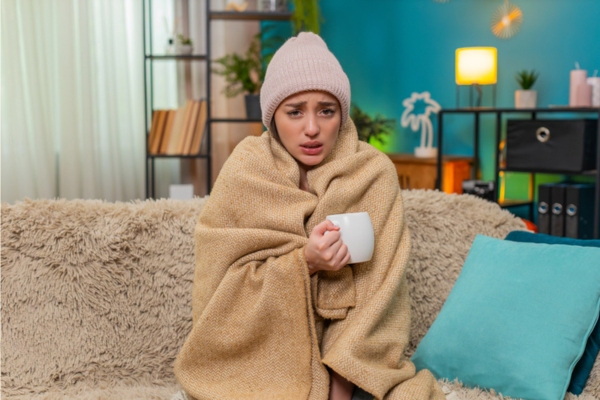 woman wrapped in blanket while having coffee and feeling cold indoor due to furnace failure