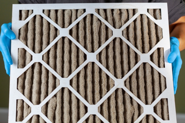 person wearing blue gloves holding dirty HVAC filter