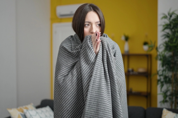 woman wrapped in blanket feeling cold at the living room due to uneven home temperature