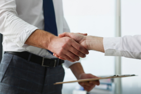 two people shaking hands with a document agreement on a clipboard
